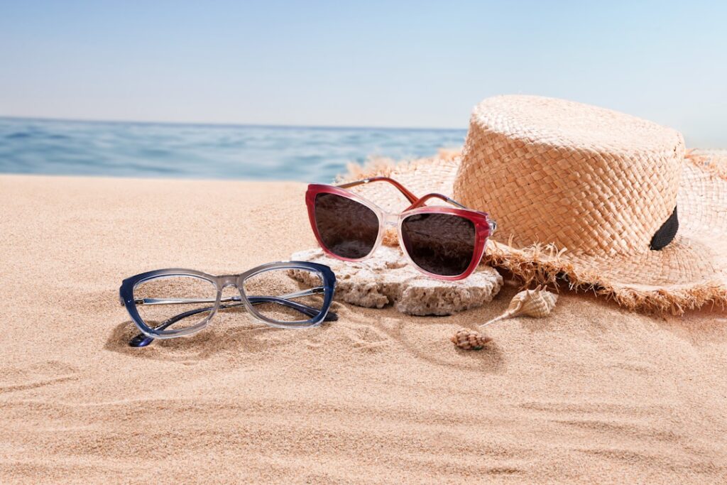 Two pairs of glasses and straw hat on beach sand.