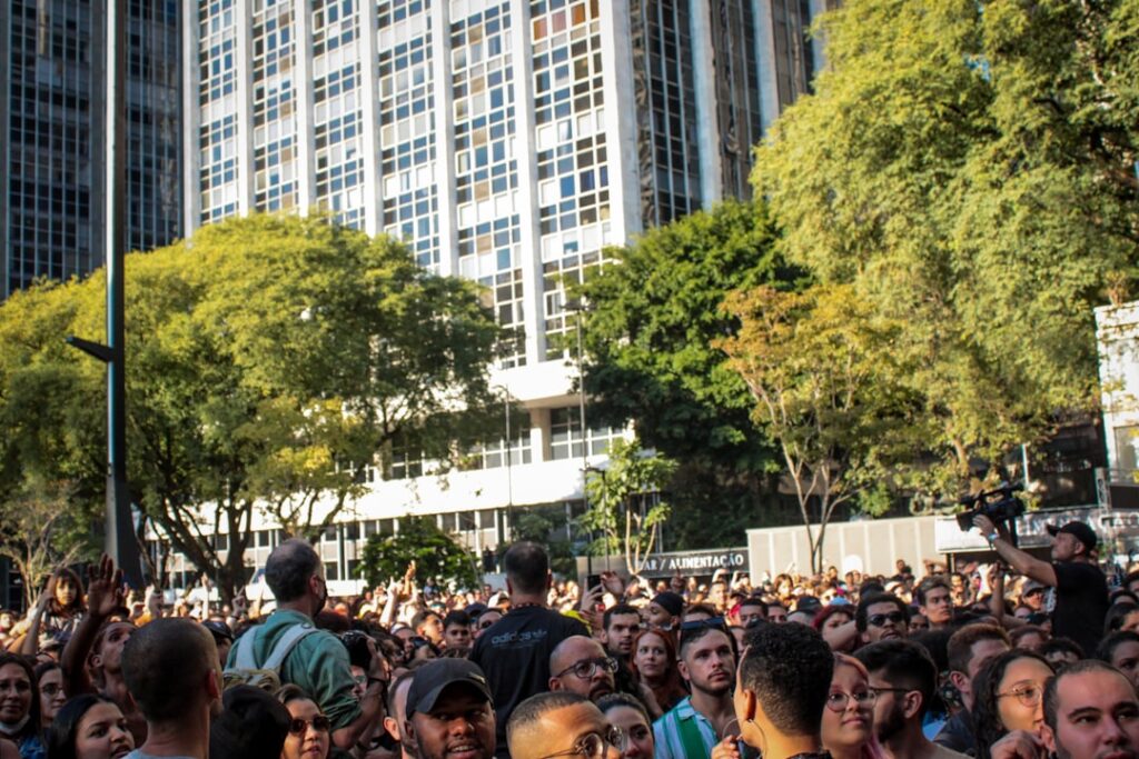 Crowd of people outdoors with tall buildings and green trees.