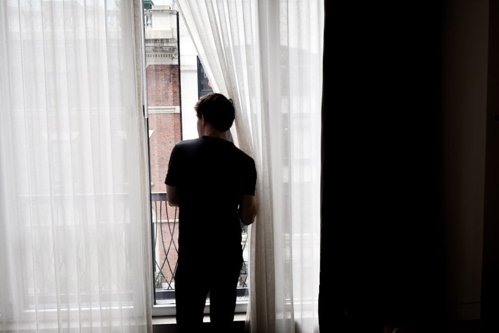 man in black crew neck t-shirt standing near white window curtain