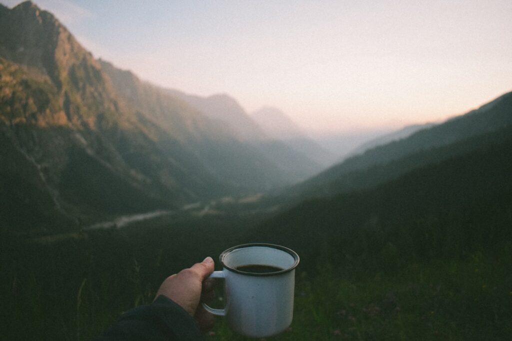 A person holding a cup of coffee in the mountains